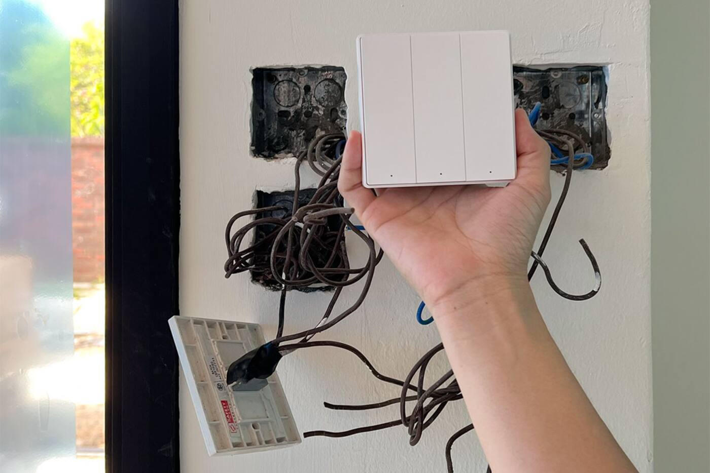 Smart wall switch held in front of open electrical switch boxes