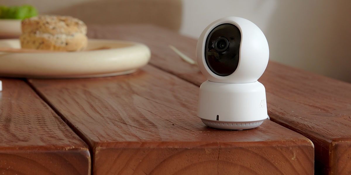 Aqara Camera E1 on a warm wooden dining table beside a breakfast plate