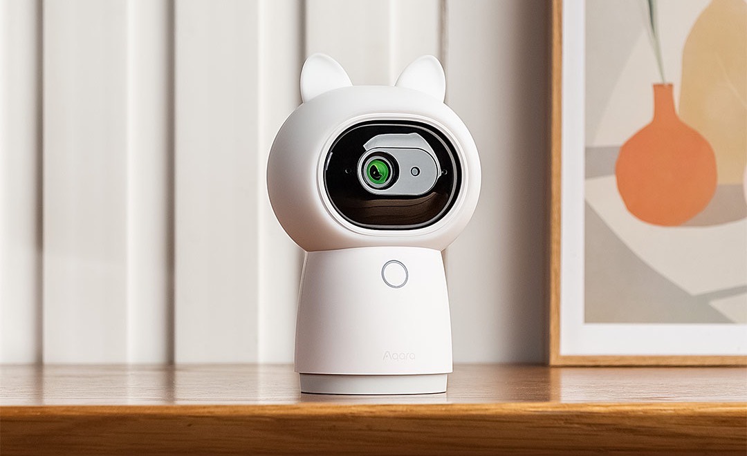Aqara Camera Hub G3 with cat-ears cover on a wooden windowsill beside a framed print