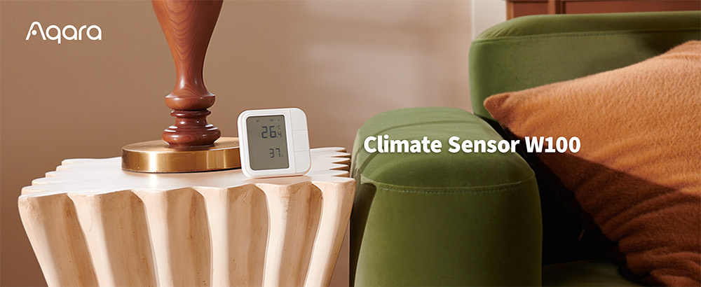 Aqara Climate Sensor W100 on a side table beside a lamp and green sofa