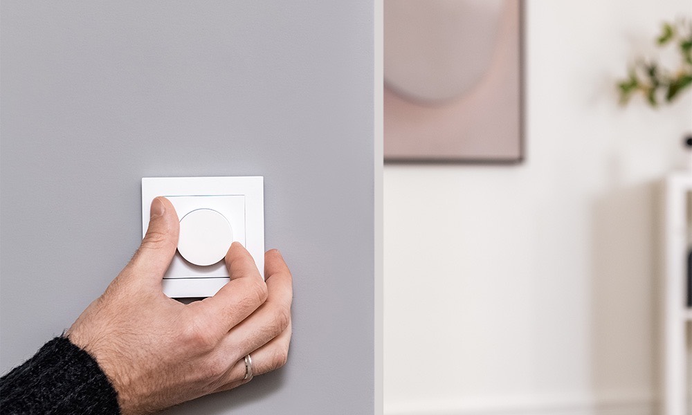 A hand turning the Aqara Dimmer Switch H2 dial on a grey living-room wall