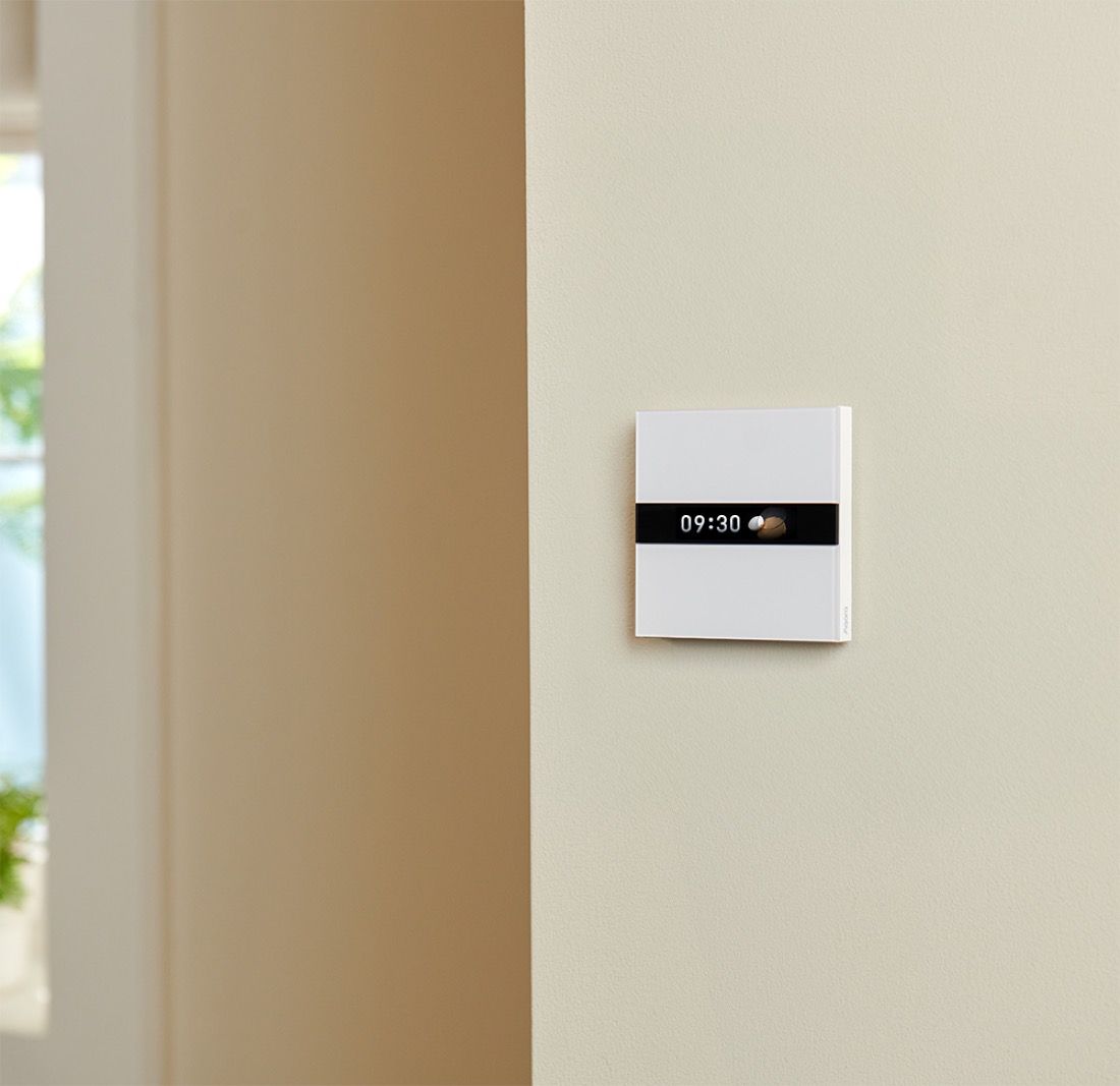Display Switch V1 mounted on a warm-lit wall, its screen showing the time