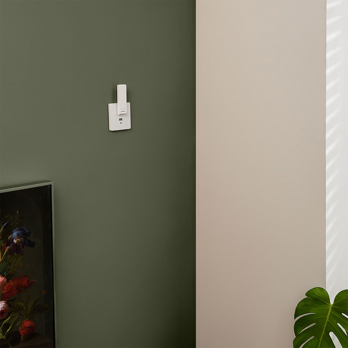 Hub E1 in a wall power socket against a deep-green wall, shaft angled outward
