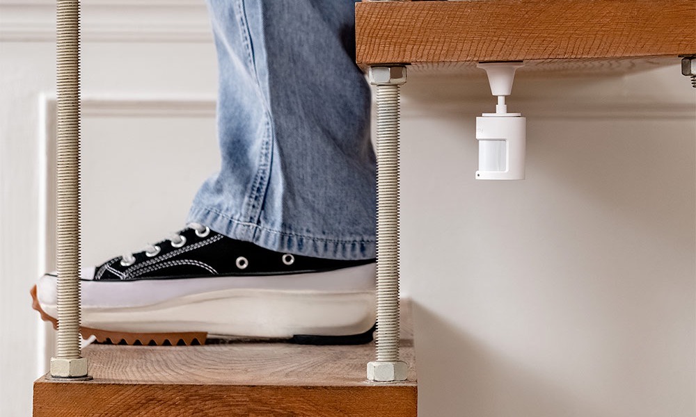 Aqara Motion Sensor P1 mounted under a floating staircase as someone climbs the steps