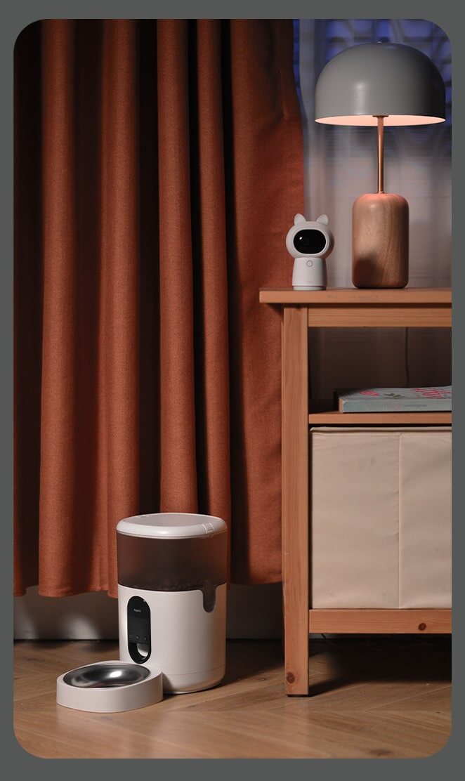 Pet Feeder C1 on the floor beside a nightstand with an Aqara camera watching over it at night