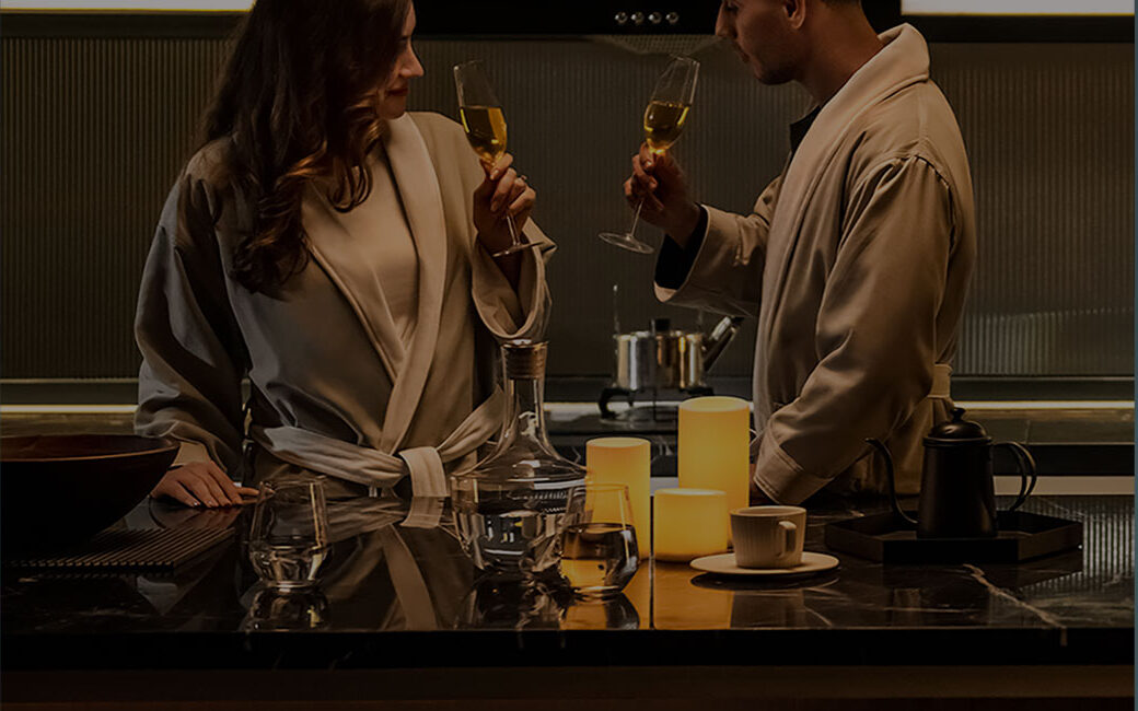 A couple in a warmly lit kitchen at night, lights and candles glowing only where they stand