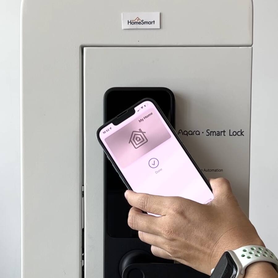 A hand tapping an iPhone with Apple Home Key to unlock the A100 mounted on a door