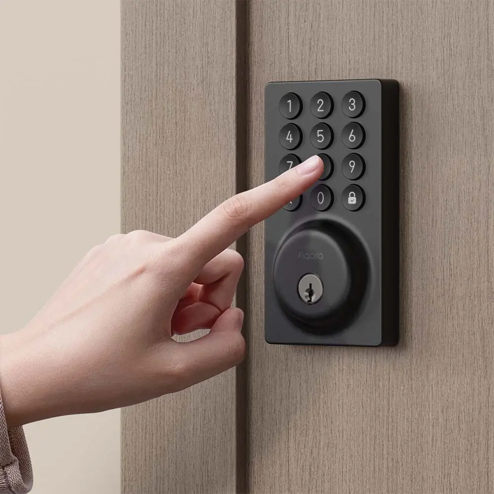 A finger entering a passcode on the backlit keypad of the Aqara Smart Lock B50 mounted on a wooden door