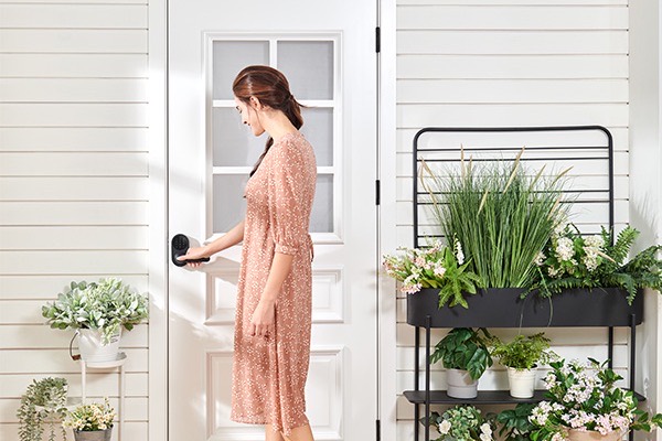 A person opening a bright home door fitted with the U300, plants and porch alongside