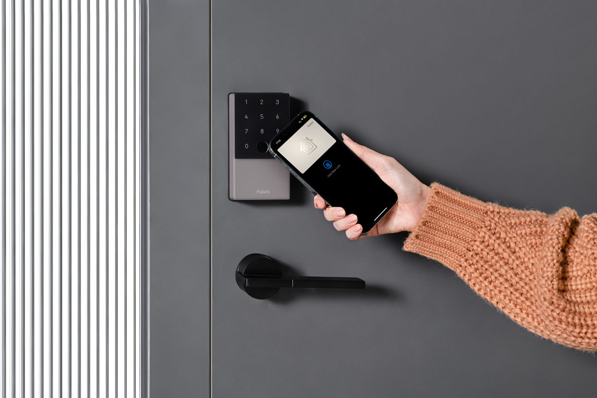 A hand holding an iPhone up to the U100 keypad to unlock the door with Apple Home Key
