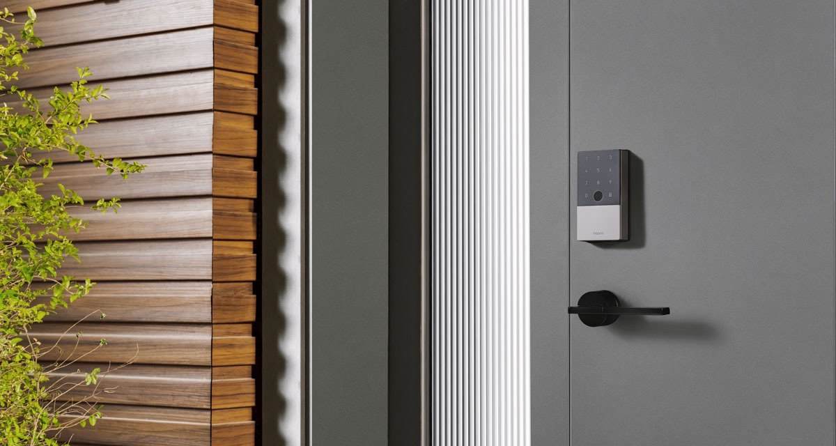 Aqara Smart Lock U100 fitted to a grey front door beside timber cladding and greenery