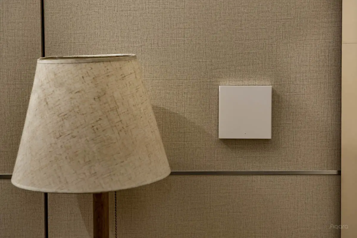 Single-rocker Wall Switch H1 mounted on a linen wall beside a lamp