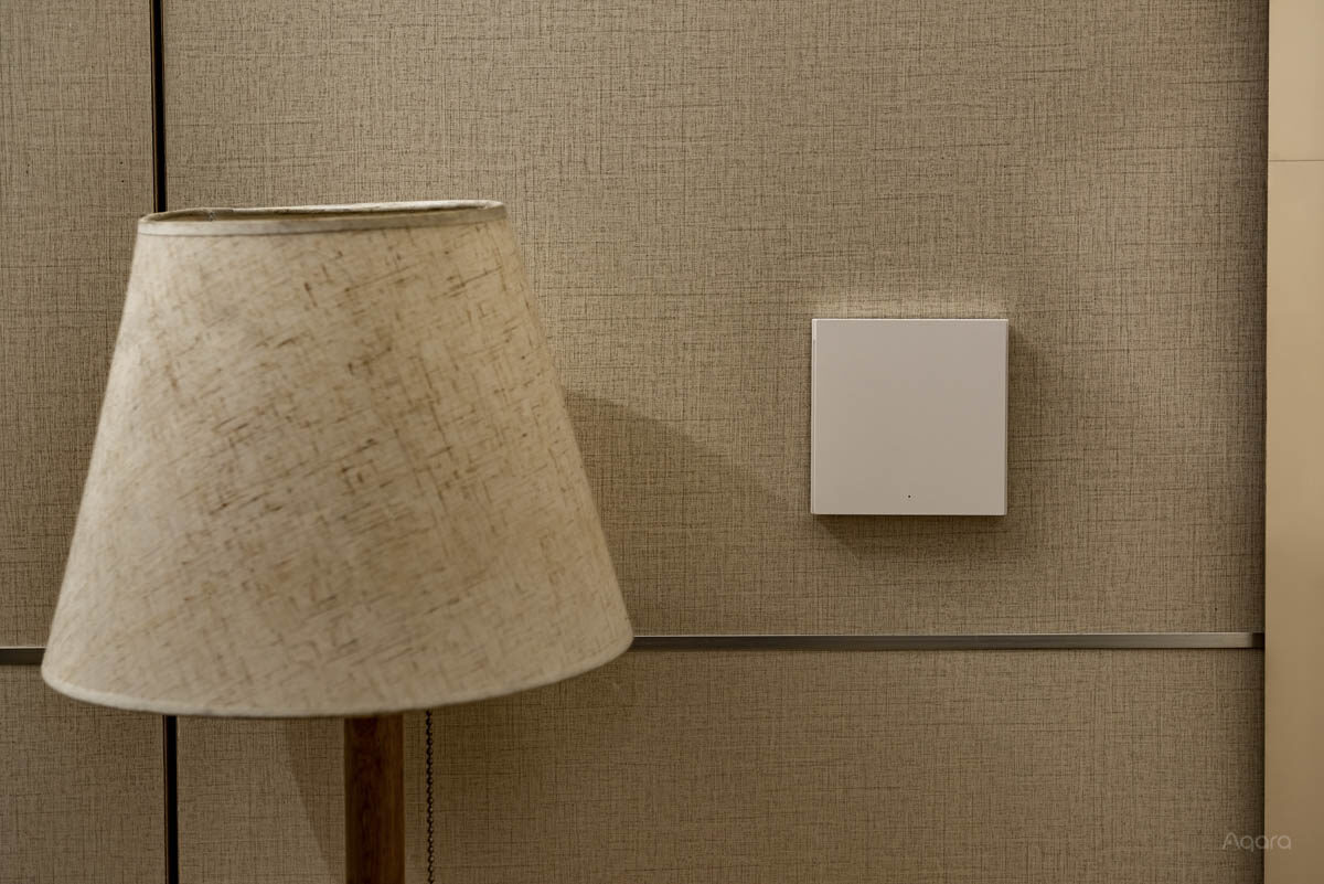 Single-rocker Wall Switch H1 mounted on a linen wall beside a lamp