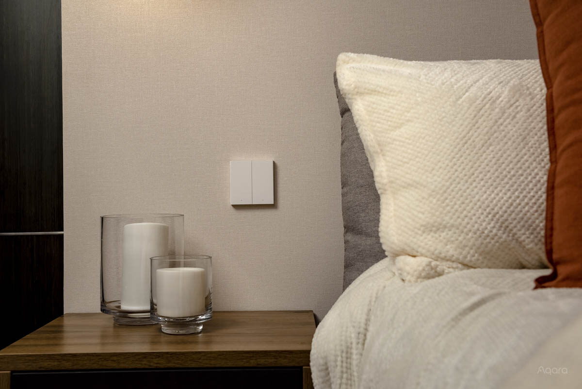 Aqara Smart Wall Switch H1 mounted beside a bed in a warmly lit bedroom