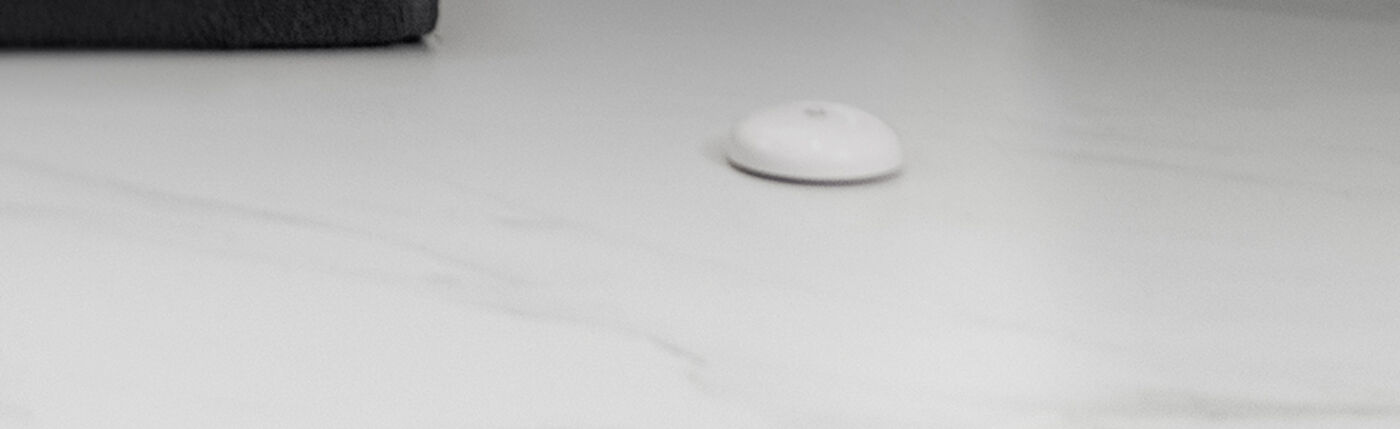Water Leak Sensor T1 sitting on a bathroom floor beside a bath mat